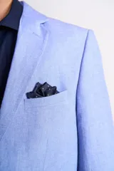 Traje de lino color beige claro, compuesto por saco de dos botones con solapa de muesca, dos bolsillos delanteros con solapa y un bolsillo en el pecho, y pantalón de vestir de corte recto. Incluye camisa blanca, corbata estampada y zapatos marrones.