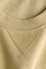 Buzo oversized color beige claro, con cuello redondo, hombros caídos y el texto "ATELIER DE MODE" en relieve con textura de felpa blanca en el frente. Cuenta con puños, cuello y dobladillo en ribete acanalado.