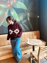 Sweater tejido color borgoña con cuello alto y diseño geométrico en el pecho en color crema.