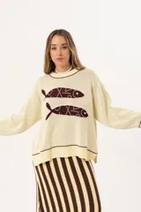 Buzo tejido de punto color crema con diseño de dos peces en color bordó en la parte frontal. Presenta detalles bordados a mano en los bordes de los peces y terminaciones con galón picot en cuello, puños y ruedo.