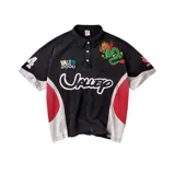Camiseta polo negra de manga corta, con cuello y cierre frontal de tres botones. Presenta diversos bordados y estampados, incluyendo la inscripción "Valley" en grande, un dragón verde y rojo en el pecho, el texto "VALE 2000", un número "4" en la manga derecha y paneles laterales en blanco y rojo.