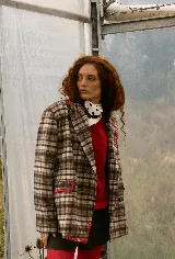 Blazer sastrero de corte oversize con estampado de cuadros en tonos tierra. Presenta cuello solapa, cierre frontal con botones, dos bolsillos laterales de vivo y detalles bordados a mano con hilo rojo en los bordes de los bolsillos, solapa y costuras. Está completamente forrado en satén.