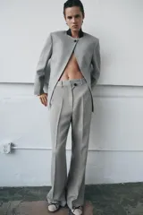 Pantalón de tiro medio con corte flare y pernera ancha. Presenta cintura con trabillas, bolsillos laterales, raya planchada frontal y cierre con cremallera, botón y ganchos metálicos.