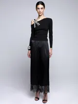 Sweater blanco de punto con escote asimétrico y manga larga. Presenta un broche con forma de moño con apliques de strass en el hombro.