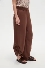 Pantalón verde militar de corte ancho y tiro alto, con cintura elástica fruncida y detalles de cordones ajustables en los tobillos.