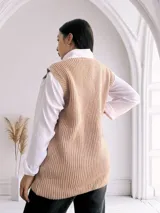 Chaleco largo de punto color beige, con cuello redondo y bolsillos frontales. Diseño sin mangas y corte recto.