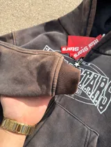 Campera canguro con cierre frontal, capucha y bolsillos tipo canguro, en tono marrón con efecto gastado vintage y estampa gráfica blanca con detalles de strass en el pecho.
