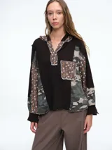 Buzo con capucha de diseño patchwork que combina paneles de tejido waffle negro, estampado camuflado y estampado floral. Presenta cierre frontal parcial con botones, bolsillo tipo parche en el pecho y mangas largas con puños.