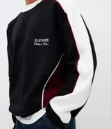 Buzo de corte boxy con diseño color block en negro, blanco y detalles en bordó. Presenta cuello redondo, mangas largas con puños acanalados y estampado lettering frontal con la frase Elevate Clothing & Culture.