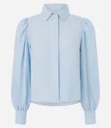 Camisa de crepé color celeste, con cuello inglés, cierre frontal oculto y mangas largas abullonadas con puños ajustados.