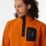 Canguro color naranja de polar fleece con cuello alto con cierre de botones a presión, bolsillo en el pecho con cierre y logo de la marca.