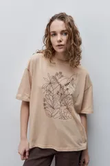 Remera negra de silueta amplia y calce relajado, con cuello redondo, mangas cortas con hombros caídos y estampa botánica en líneas blancas en el frente.