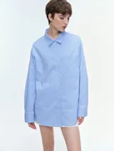 Camisa oversize de popelina de algodón con diseño de rayas verticales, cuello clásico, cierre frontal con botones, manga larga con puños anchos y bolsillo aplicado en el pecho.