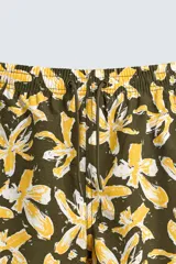 Bañador de hombre con estampado floral en tonos amarillo y blanco sobre fondo verde oliva. Presenta cintura elástica ajustable con cordón, bolsillos frontales y forro interior.
