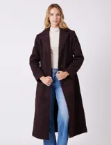 Tapado largo de bouclé color marrón oscuro, con silueta entallada que termina en evasé. Tiene cuello de solapa amplia, cierre frontal con tres botones a tono y bolsillos funcionales con solapa. Incluye forro interno a tono.