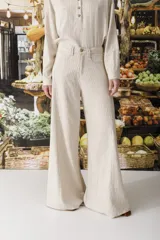 Pantalón de tiro alto, pierna ancha y largo, color beige claro con finas rayas verticales en tono oscuro. Presenta un diseño de cinco bolsillos estilo jean.