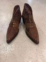 Botas cortas de cuero color chocolate con acabado desgastado y detalle de tachas metálicas. Presentan un taco cuadrado de madera y punta fina.