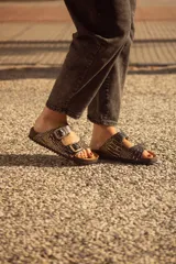 Sandalias de cuero sintético con estampado de piel de cocodrilo en tonos negro y dorado, con dos hebillas doradas ajustables y plantilla anatómica de corcho.