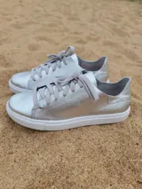 Zapatillas plateadas de cuero con cordones grises y suela blanca.