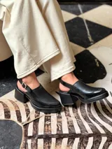 Zapato tipo slingback color negro, con plataforma y taco cuadrado. Presenta una puntera cuadrada y cierre con hebilla metálica en la tira trasera.