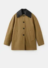 Chaqueta de corte amplio en tono tostado, con solapas y cuello de cuero sintético en color negro kontrastante. Posee cierre frontal de botones oscuros y bolsillos laterales discretos.