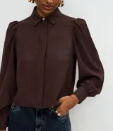 Camisa de crepé color celeste, con cuello inglés, manga larga abullonada y cierre frontal oculto con botón diferenciado en el cuello.