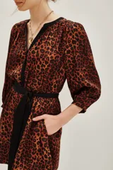 Vestido corto de estilo camisero con estampado animal print en tonos caramelo y negro. Presenta cuello en V con solapas negras, mangas tres cuartos y un lazo negro ajustable en la cintura para entallar la silueta.