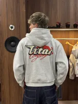 Buzo con capucha gris jaspeado, de corte holgado, con estampado gráfico en la espalda que incluye el texto 'Ittai Company' y una figura de un animal en color rojo.