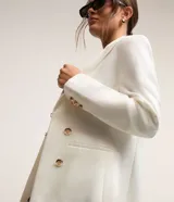 Blazer blanco de punto roma con cuello solapa, corte sastrero alargado, bolsillos y cierre con corchete.
