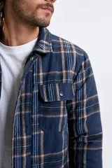 Sobrecamisa de franela a cuadros en tonos azul marino y beige, con cierre frontal de cremallera, bolsillos superiores con solapa y bolsillos laterales.
