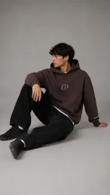 Hoodie color marrón chocolate con capucha, bolsillo frontal tipo canguro y logo bordado en el pecho con diseño de letra D estilizada.