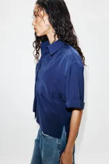 Camisa de cuello solapa y manga corta con dobladillo, presenta bolsillos de plastrón en el frente, bajo asimétrico y cierre frontal con botones ocultos.