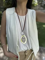 Collar largo con cordón de cuero marrón, dije circular plateado y dije ovalado con marco dorado y centro con diseño abstracto.