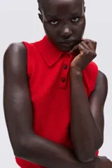 Chaleco corto de punto rojo vibrante, con cuello camisero y tapeta de tres botones oscuros. Presenta un tejido suave y ligeramente texturado, con ribetes acanalados en las sisas y el bajo.