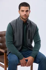 Chaleco deportivo de polar color gris, con cuello alto, cierre frontal completo y ribetes negros en sisas y bordes. Cuenta con un bolsillo vertical con cierre en el pecho.