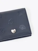 Mini billetera de cuero vacuno color rojo, con diseño grabado de pequeñas mariquitas en el frente y un aplique metálico en forma de corazón. Cuenta con un interior funcional con espacios organizadores para tarjetas.