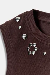 Camiseta sin mangas de tejido rib color marrón chocolate, con cuello redondo y detalle de tachas metálicas decorativas en la parte frontal superior.
