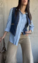 Chaleco de denim azul oscuro con detalles de costuras decorativas y ribetes en tono tostado.