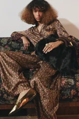 Maxi bolso de mano con acabado de pelo sintético en color marrón oscuro. Presenta un diseño estructurado con doble asa de mano reforzada y detalles metálicos dorados en las uniones. Cuenta con cierre mediante botón imantado y forro interior con bolsillo con cremallera.