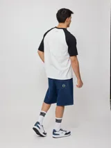 Remera blanca con mangas raglán negras y estampado frontal con el logo de Rusty en azul.