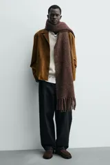 Mocasín de vestir para hombre, fabricado en piel con acabado serraje (gamuza) color marrón oscuro/café. Presenta un detalle de antifaz en el empeine con costuras visibles y horma cuadrada. La suela es negra y a contraste con un ligero tacón.