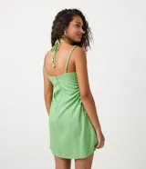 Vestido corto verde de lino con tirantes finos ajustables, escote halter con lazo y cutouts laterales con lazos.