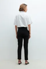 Pantalón negro de vestir, corte recto y tiro alto, con puños doblados. Se ajusta a la cintura con un cinturón fino de hebilla metálica con forma de doble 'X' o infinito.