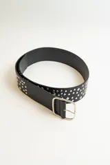 Cinturón negro de cuero sintético con tachas metálicas plateadas distribuidas en toda la superficie y hebilla metálica cuadrada.