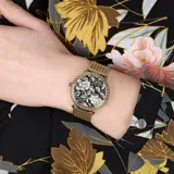Reloj GUESS modelo Willow con caja redonda dorada de 36mm, bisel con piedras blancas y esfera negra con diseño floral en blanco. Malla metálica dorada y cristal mineral resistente. Resistente al agua hasta 3 ATM.