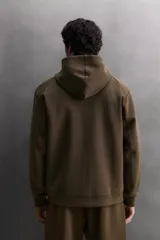 Sudadera con capucha de entrenamiento, confeccionada en tejido técnico de algodón con efecto neopreno. Presenta cierre frontal de cremallera, cuello subido, bolsillos laterales y un bolsillo en el pecho, todos con cierre de cremallera y acabado termofijado.