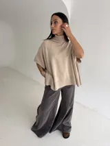 Poncho de tejido de punto color beige, con cuello alto tipo polera, diseño holgado y terminación en rib acanalado en el ruedo.