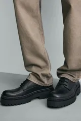 Zapato de vestir tipo derby, color negro, con parte superior lisa, horma redonda, suela con plataforma y piso track.