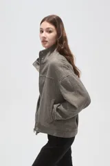 Campera de corte holgado en color gris, con cuello alto, cierre frontal oculto y mangas largas. Presenta costuras decorativas en el frente y bolsillos laterales.