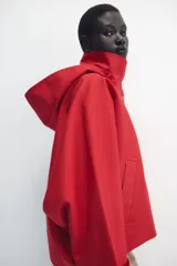 Cazadora roja de cuello subido con capucha y manga larga, bolsillos delanteros y cierre frontal cruzado con botones a presión dorados.